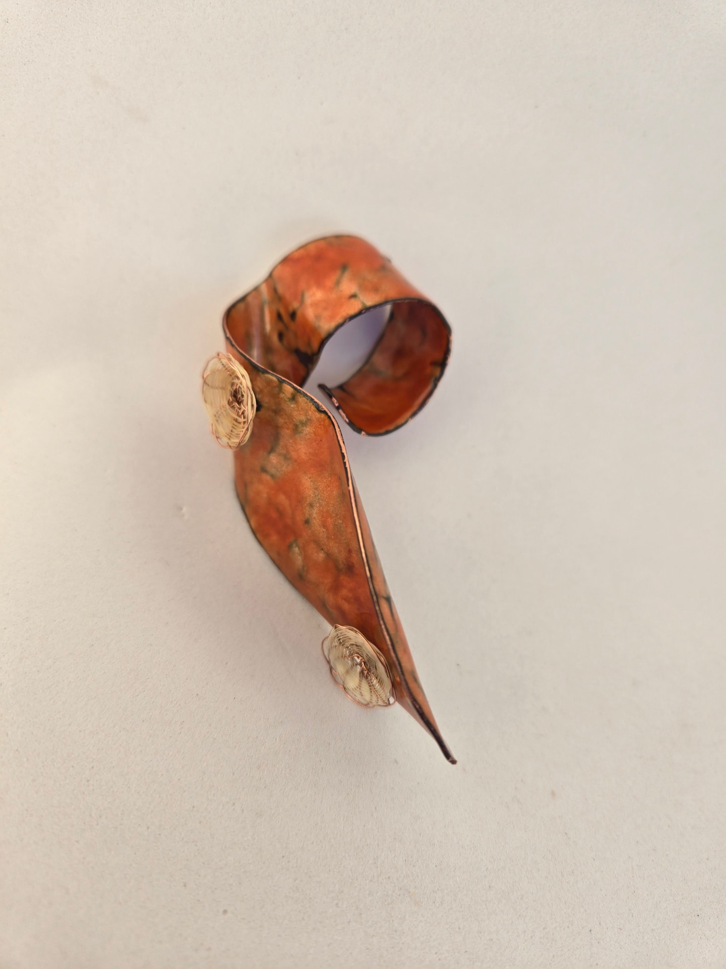 Pieza alargada en cobre y naranja con alambres, sobre una superficie clara y texturada.