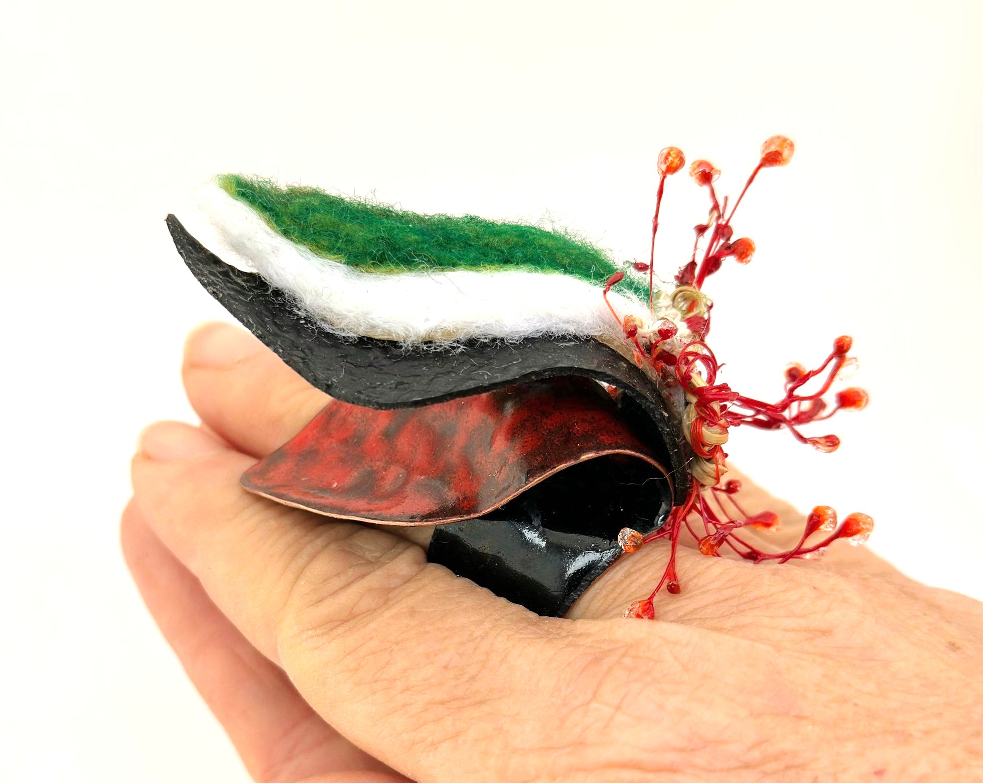 Pieza escultórica en negro, rojo, verde y blanco sostenida en la mano.